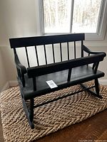 Full view of black wooden nanny bench on woven mat, showing overall form