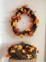 Two decorated grapevine wreaths displayed vertically on wall, showing foliage details