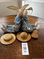 Both bunnies seated back-to-back with three straw hats in foreground