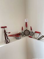 All seven red-handled metal kitchen utensils displayed together