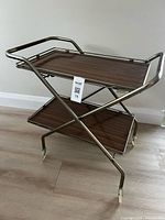 Full view of metal X-frame bar cart with two wood-grain shelves and casters