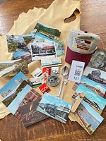 All items spread out on table including postcards, matchbooks, cap, belt buckle, cutlery, whistle