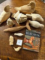 Group shot of ten unfinished wood carvings and woodworking book on table