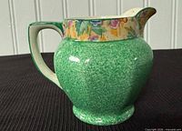Left side view of green speckled porcelain cream jug with floral band