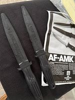 Two black AF-AMK rubber training knives on chair with literature