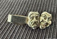 Front view of gold-tone tie clip with tragedy and comedy masks
