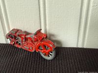 Left side view of red cast lead motorcycle toy against white panel