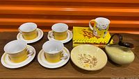 Full lot view showing yellow Mikasa cups and saucers, Woods Ware bowl, German creamer, mug, and two books