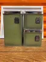 Three avocado green metal canisters front view showing letter badges