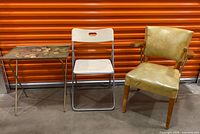 Front view of TV tray, folding chair, vinyl arm chair against orange backdrop