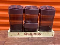 Three tall and one short smoked brown canisters with lids seated in original box