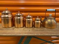 Full view of four copper canisters and kettle on shelf