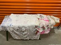 All items on table: white quilt, pink patchwork blanket, doilies
