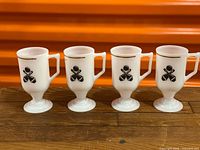 Front view of four milk glass pedestal mugs showing bowling logos and gold rim