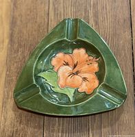 Top view of triangular Moorcroft ashtray showing green glaze and orange hibiscus motif