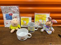 Full lot showing both plush dolls, two mugs, two napkin packs, and sealed gift wrap