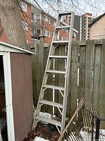 Full view of aluminum step ladder leaning against wooden fence