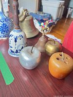 Group shot showing ceramic bell, cast iron bell, brass bell, three apple accessories, glass vase partially