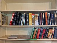 Three shelves of assorted hardcover and paperback books including large reference volumes and smaller novels