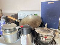 Overview of cookware on stove: wok, kettle, pot with lid, carafe, cutting board