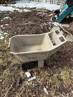 Full view of beige resin garden cart outdoors on soil and snow