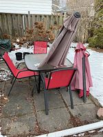 Patio table with red chairs, folded umbrella atop table, snow background