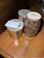 Two plastic cans and one glass jar filled with pennies on table