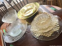 Group of mixed glassware on table including Pyrex bowl, leaf platter, frosted bowls, swirl plates and pressed-glass pieces