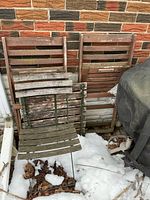 Three folding wooden slat chairs leaning against brick wall with one slat tabletop in front