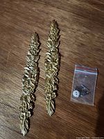 Pair of brass appliques with bag of screws on wood surface