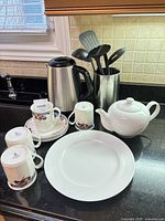 Group shot of all items on countertop including kettle, cups, saucers, plate, teapot and utensil holder