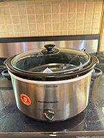 Front view of Hamilton Beach slow cooker showing stainless steel exterior, glass lid and control dial