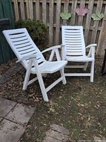 Both white resin folding lounge chairs side by side outdoors