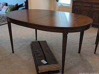 Full view of oval dining table with leaves in sleeves on floor
