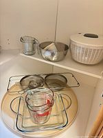 Shelf view showing salad spinner, mixing bowl, sieves, glass baking dishes, measuring cups and lazy susan