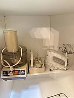GE food processor base, accessory rack, Braun hand mixer with attachments on shelf