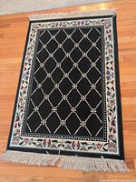 Full view of rectangular black rug with fringe and patterned border