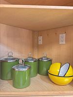 Four green canisters and three yellow bowls on shelf