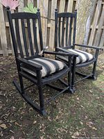 Both black resin rocking chairs with striped cushions on ground