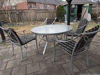 Round glass-top patio table with four matching chairs on patio