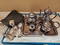 Group shot of entire silver plated tea service, tray, goblets, shakers, felt bag