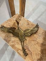 Full view of brass bird sculpture on plywood surface