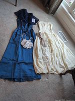 Blue gown, cream gown, gloves and beaded purse laid out on floor