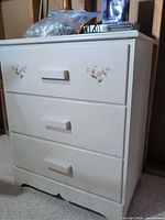 Front view of white painted nightstand with three drawers and floral stencils