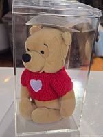 Front view of Pooh plush in display case showing sweater with heart