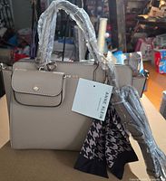 Front view of tote with hangtag, scarf, protective wrap on handles