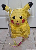 Front view of yellow Pikachu piñata showing face, tag and pull strings