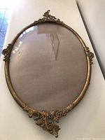 Full view of oval frame showing ornate crest, bubble glass and lower embellishment