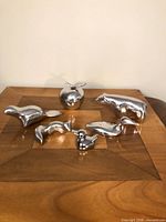 Group shot of six polished aluminum figurines on wood surface