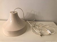 Full view of beige painted metal pendant lamp with cord and switch